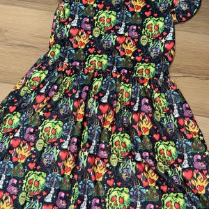 May include: A black dress with a colorful print featuring cartoon characters, hearts, and flames. The dress has short sleeves with ruffled edges and a gathered waist. The print includes green, red, yellow, and purple elements.