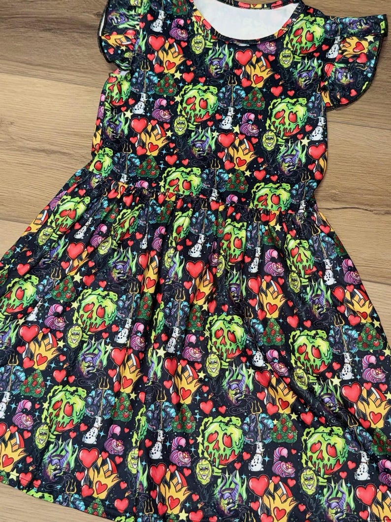 May include: A black dress with a colorful print featuring cartoon characters, hearts, and flames. The dress has short sleeves with ruffled edges and a gathered waist. The print includes green, red, yellow, and purple elements.