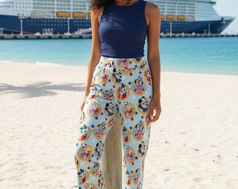 May include: A woman wearing a navy blue tank top and light blue pajama pants. The pajama pants have a repeating pattern of Mickey Mouse, Minnie Mouse, and other Disney characters. The background includes a beach, ocean, and a cruise ship.
