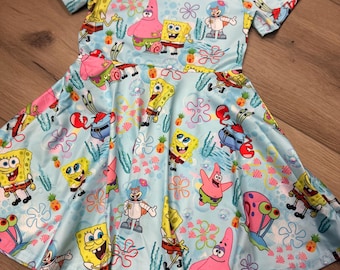 May include: A light blue dress featuring a repeating pattern of SpongeBob SquarePants and his friends. The dress has short sleeves and a flared skirt. The characters are in various poses, surrounded by flowers and other aquatic elements.