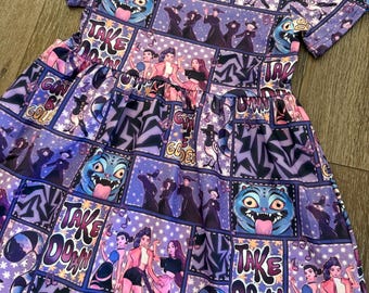 May include: A purple dress with a comic book style print featuring illustrations of characters, text, and starburst patterns. The dress has short sleeves and a flared skirt. The text includes phrases like "Take Down" and "Gonna Be Golden".