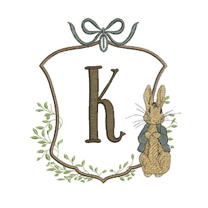 May include: An embroidered design featuring the letter "K" in a brown shield shape, surrounded by green leaves and a bow. A cartoon rabbit wearing a blue jacket is on the right. The design is available in 4 sizes, ranging from 4.7 to 7.5 inches.