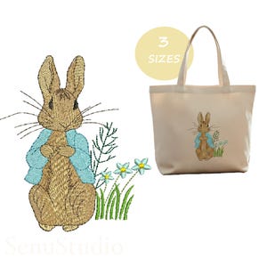 May include: An embroidered design featuring a rabbit in a blue jacket, with flowers and grass, is displayed on a tote bag. The design is also shown as a digital embroidery file. The bag is beige and has a handle.
