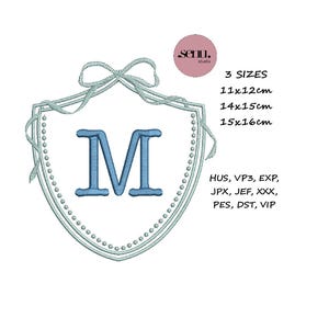 May include: A light blue embroidered shield design with the letter "M" in the center. The shield is surrounded by a dotted border and a bow at the top. Text on the right indicates three sizes: 11x12cm, 14x15cm, and 15x16cm.