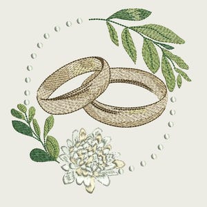 Pode incluir: Design bordado com duas alianças de casamento douradas entrelaçadas, rodeadas por folhas verdes, uma flor branca e uma borda pontilhada sobre um fundo creme. O design evoca romance e celebração.