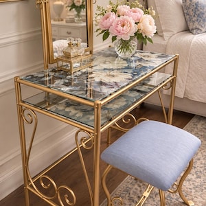 May include: A gold metal vanity table with two glass shelves featuring a floral print, an arched swivel mirror, and a matching stool with a light blue upholstered seat. A glass vase with pink peonies sits on the top shelf next to a small glass box.