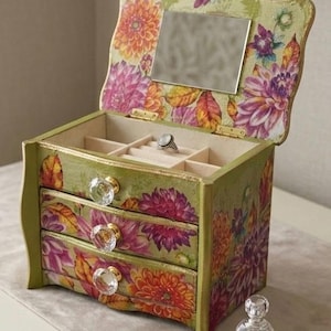 May include: A green wooden jewelry box with three drawers and a hinged lid. The box is decorated with a floral pattern in shades of orange, pink, and purple. The drawers have crystal knobs. The lid has a small mirror inside.