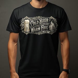 May include: Black t-shirt featuring a decorative design with the words "Cold Beer Warm Fire" in a vintage style. The design includes a beer stein and a flame. The shirt is made of a soft material.