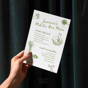 May include: A white menu titled "Jasmine's Matcha Bar Menu" with green text and illustrations. The menu lists matcha drinks and sweet and savory bites. The menu is held by a person.