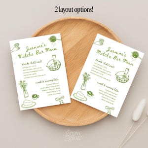 May include: Two white menu cards with green illustrations and text, labeled "Jasmine's Matcha Bar Menu." The menu lists drink and food options, including matcha lattes and savory bites. The cards are on a wooden tray.