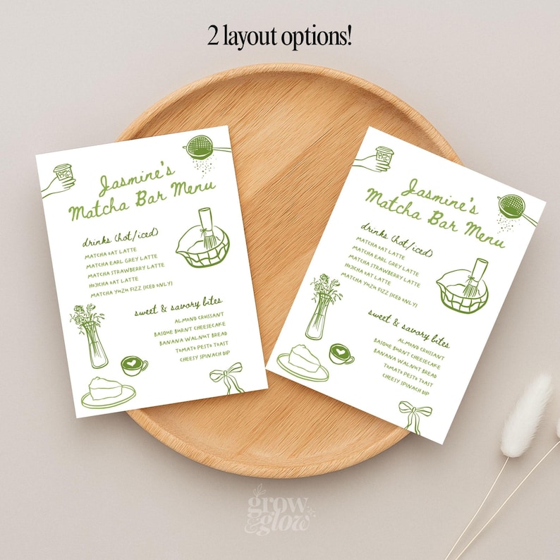 May include: Two white menu cards with green illustrations and text, labeled "Jasmine's Matcha Bar Menu." The menu lists drink and food options, including matcha lattes and savory bites. The cards are on a wooden tray.