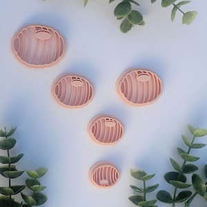 May include: Set of four pink plastic cookie cutters shaped like a bun with a swirl design. The cutters are arranged in a pyramid shape on a white background.