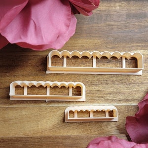 May include: Three plastic cookie cutters in different sizes, all with a scalloped edge design. The cutters are on a wooden surface.