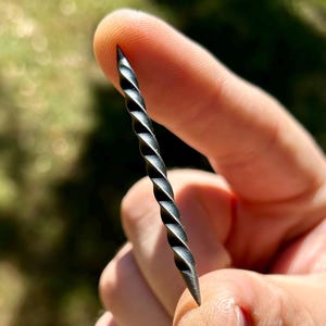 May include: A close-up of a twisted metal rod with a sharp point. The rod is held by a finger and thumb.