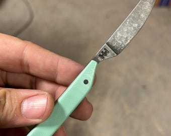 May include: A small, sharp knife with a textured, silver-colored blade and a mint green handle. The handle has two black rivets. The blade has a logo etched into it. The knife is designed for precision cutting.