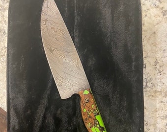 May include: A Damascus steel chef's knife with a green and brown patterned handle. The knife is in a black zippered case.