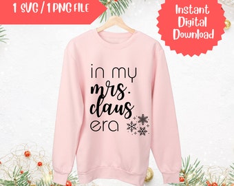 Op de afbeelding: Roze sweatshirt met de tekst "in my mrs. claus era" in zwarte letters met sneeuwvlokken.