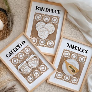 Puede incluir: Tres impresiones enmarcadas con las palabras "PAN DULCE", "CAFECITO" y "TAMALES" en texto negro. Cada impresión presenta un fondo marrón con patrones florales blancos e ilustraciones de pasteles y comida mexicanos. Los marcos son de color marrón claro.
