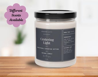 Pode incluir: Um frasco de vela de vidro transparente com uma tampa preta. O rótulo é azul escuro com texto branco que diz "Centering Light", "Meditation & Intention Setting", "Natural Candle" e "Wedgeport Gifts". A vela é de 9 oz e tem um tempo de queima de 50 a 60 horas.