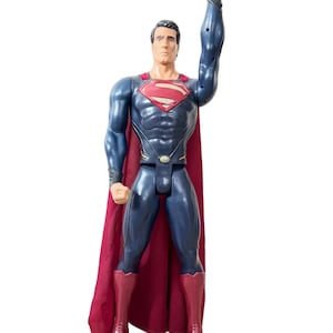 May include: A blue and red Superman action figure with a red cape. The figure is standing with its right arm raised in a fist.