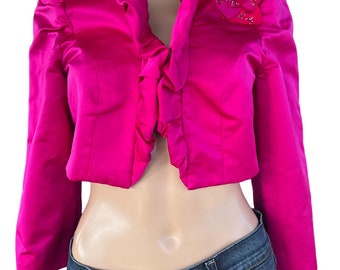 May include: A hot pink satin cropped jacket with a ruffled collar and a beaded flower detail on the right shoulder.