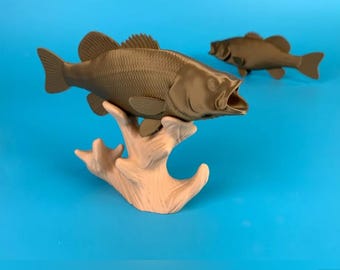 Op de afbeelding: Twee bruine 3D-geprinte baarsvisjes. Eén visje zit op een lichtbruine 3D-geprinte boomtakstandaard. Het andere visje bevindt zich op een blauw oppervlak.