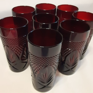 May include: A set of eight ruby red drinking glasses. The glasses have a diamond pattern and leaf design. The glasses are cylindrical with a thick rim and are made of glass.