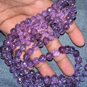 May include: A strand of purple faceted gemstone beads. The beads are round and have a shiny, iridescent finish.