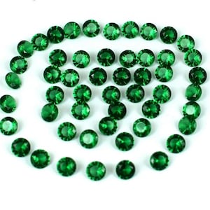 Puede incluir: Colección de gemas redondas facetadas de color verde esmeralda dispuestas en espiral sobre un fondo blanco. Las gemas son de tamaño uniforme y muestran una calidad brillante y reflectante, lo que sugiere alta claridad y corte.