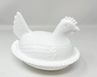 May include: White ceramic chicken shaped butter dish with a detailed design. The chicken is sitting in a nest with a beaded edge.