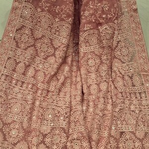 May include: A pink sheer shawl with intricate embroidery and mirror work. The shawl has a floral pattern and a border with tassels.