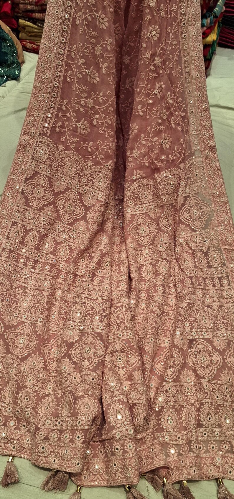 May include: A pink sheer shawl with intricate embroidery and mirror work. The shawl has a floral pattern and a border with tassels.