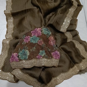 May include: A brown silk saree with a floral print and a sequined border. The saree has a scalloped edge and is decorated with small sequins.