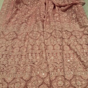 May include: A pink chiffon saree with white embroidery and mirror work. The saree has a floral design and a border with tassels.