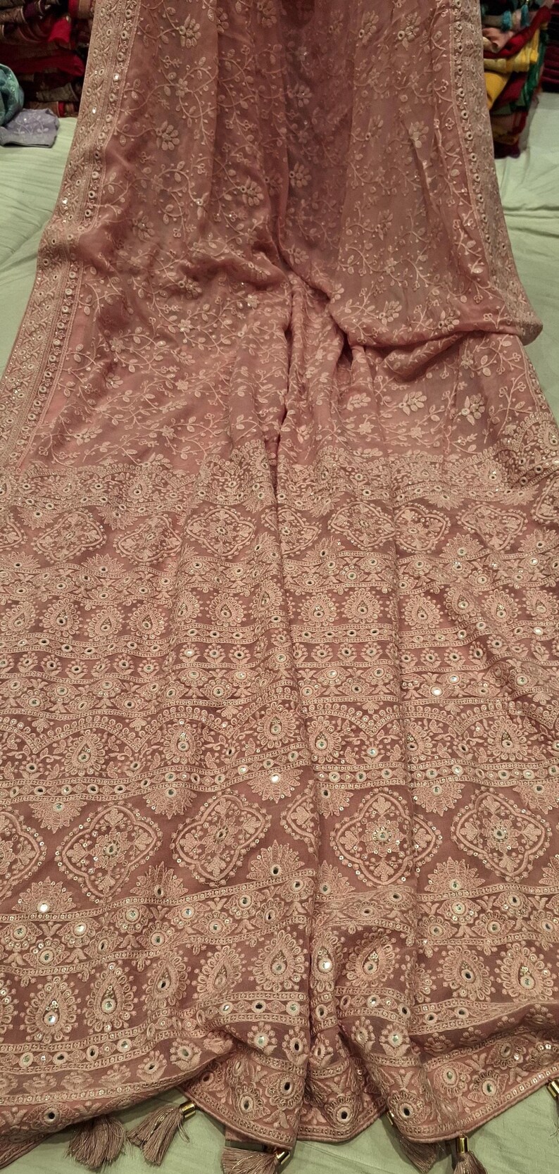 May include: A pink chiffon saree with white embroidery and mirror work. The saree has a floral design and a border with tassels.