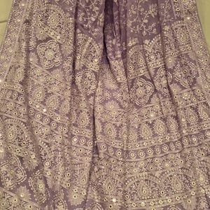 May include: A lilac sheer shawl with intricate white embroidery and silver mirror work. The shawl has a border with a repeating pattern of silver sequins and mirror work.