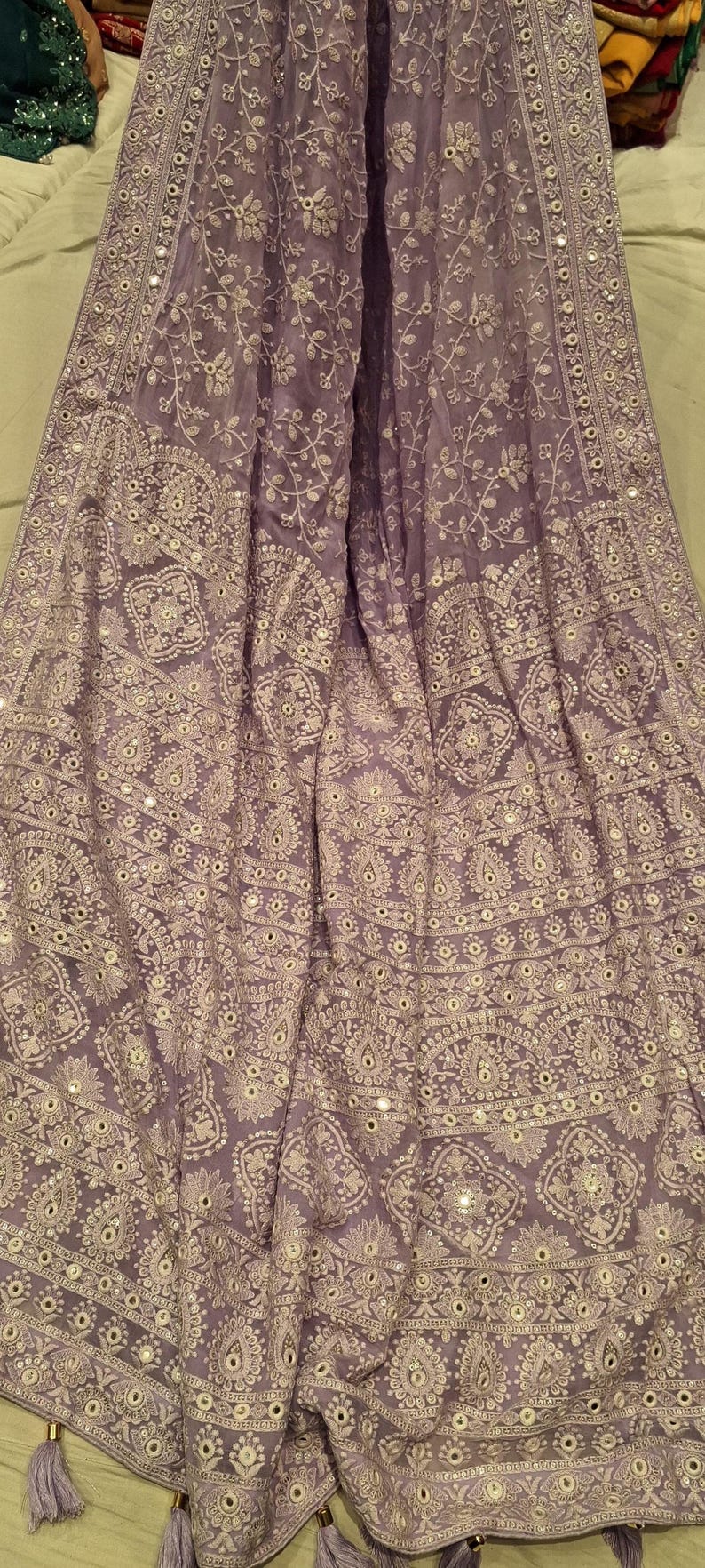 May include: A lilac sheer shawl with intricate white embroidery and silver mirror work. The shawl has a border with a repeating pattern of silver sequins and mirror work.