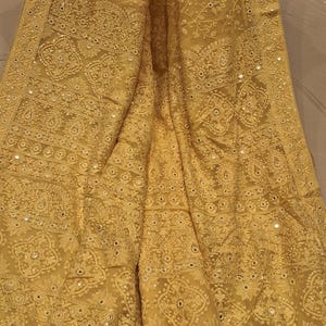 May include: A yellow chiffon saree with intricate embroidery and mirror work. The saree has a delicate floral pattern and a border with a geometric design. The saree is adorned with small, round mirrors that add a touch of sparkle.