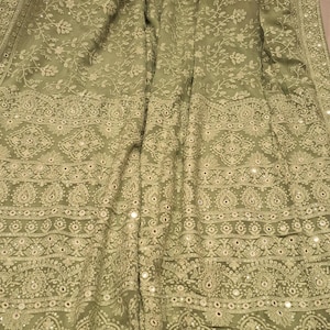 May include: A sage green chiffon saree with intricate floral embroidery and mirror work. The saree has a border with a repeating pattern of paisley motifs and sequins.