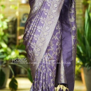 May include: A lavender Munga crepe silk saree with muted gold jaal weaving. The saree features intricate floral patterns and a decorative border. The text "HS3805" is visible on the image.