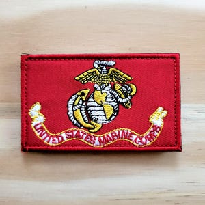 May include: Embroidered patch featuring the United States Marine Corps emblem on a red rectangular background. The emblem includes an eagle, globe, and anchor design, with "UNITED STATES MARINE CORPS" in a curved banner.