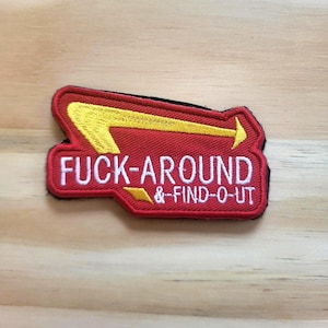 May include: Embroidered patch with the text "FUCK-AROUND & -FIND-O-UT" in white, set against a red background. The patch features a yellow arrow design. The patch is rectangular with a black border.