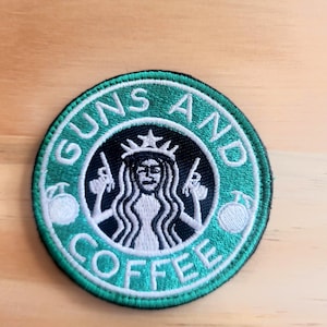 May include: Round embroidered patch with a green border and the words "GUNS AND COFFEE" in white. The central design features a woman with a crown, holding guns, in a black circle. Two white coffee bean designs are on either side.