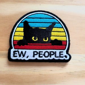 May include: Embroidered patch featuring a black cat peeking over a red line, with a retro sunset design in yellow, blue, and white. The text "EW, PEOPLE" is displayed in white on a black background.
