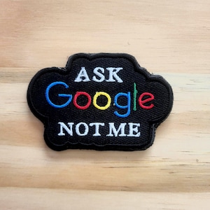 May include: Black embroidered patch with the text "ASK Google NOT ME". The word "Google" is in the Google logo colors: blue, red, yellow, and green. The patch has a black border and a cloud shape.