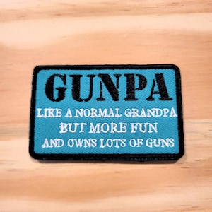 May include: A rectangular patch with a black border and a teal blue center. The patch reads "GUNPA" in large black letters, followed by text that says "LIKE A NORMAL GRANDPA BUT MORE FUN AND OWNS LOTS OF GUNS."
