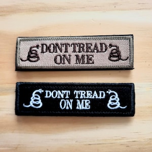 May include: Two rectangular embroidered patches. One is tan with brown text and a coiled snake, the other is black with white text and a white snake. Both read "DON'T TREAD ON ME".
