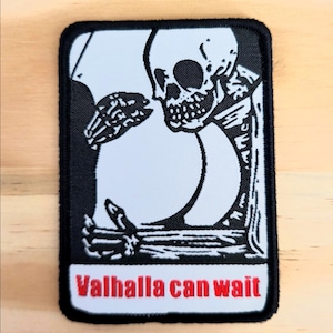 Puede incluir: Parche en blanco y negro con un esqueleto y un gran c&iacute;rculo blanco. El esqueleto toca el c&iacute;rculo con su mano &oacute;sea. El texto "Valhalla can wait" est&aacute; en rojo en la parte inferior del parche.