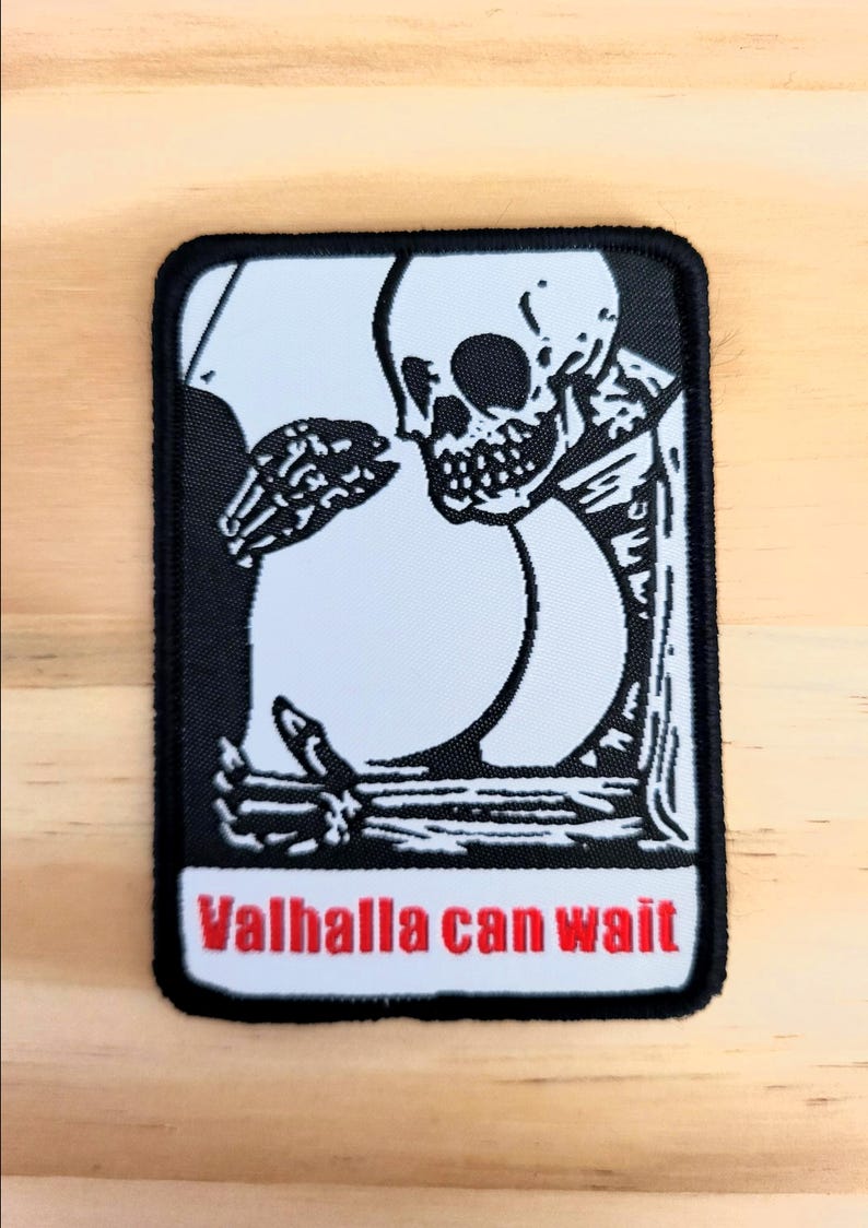 Puede incluir: Parche en blanco y negro con un esqueleto y un gran c&iacute;rculo blanco. El esqueleto toca el c&iacute;rculo con su mano &oacute;sea. El texto "Valhalla can wait" est&aacute; en rojo en la parte inferior del parche.