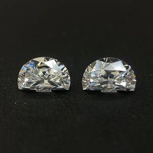 Puede incluir: Dos gemas talladas en media luna con facetas brillantes, que reflejan la luz. Las gemas son claras y brillantes, sobre un fondo oscuro. El texto "NIKSMODA" es visible en cada gema.